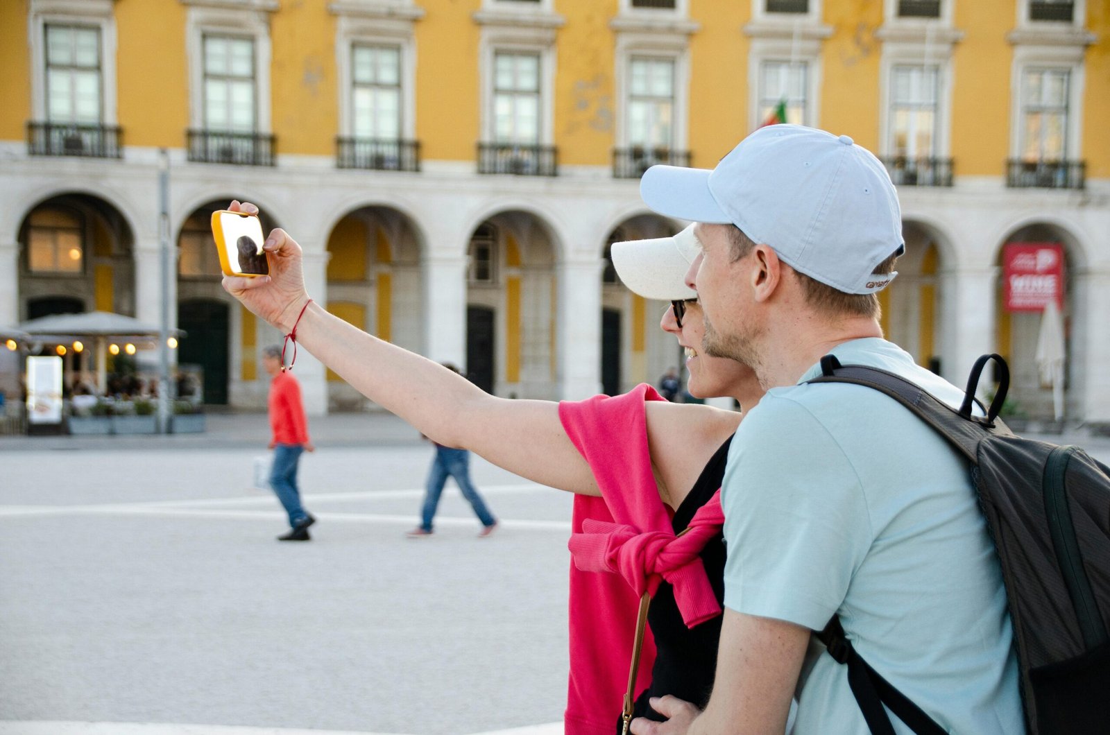 A couple takes a selfie in front of the iconic Praça do Comércio in Lisbon, showcasing historic architecture.